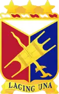 A Gold color metal and enamel device 1+1⁄4 inches (3.2 cm) consisting of a shield blazoned: Per pall Argent, Gules and Azure, over the second and third an Igorot war shield and kris in saltire Or. Attached above the shield a wreath of the colors Argent and Gules three mullets Or. Attached below the shield a Gold scroll inscribed 'LAGING UNA' in Blue letters.