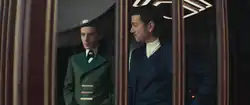 Cassian and Thela look out of the hotel room window onto the Palmo Plaza