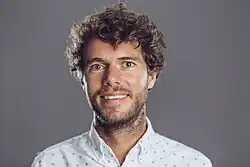 A white man in his 30s, with brown hair, smiling awkwardly at the camera.