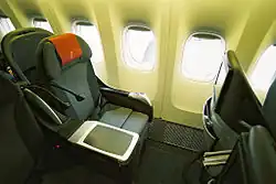 A dark grey colored seat with red headrest cover, with unshaded windows on the right