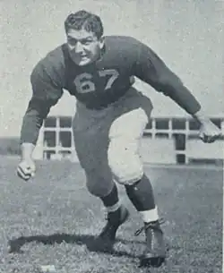 A black and white photo of Pregulman in uniform posing like he is about to block or tackle someone