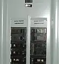 Illustration of breaker numbering in a North American type panelboard. Some labels are missing, and some are additional. The numbers on the toggles indicate the rated amperage before tripping. The top right breaker (Rated at 100&nbsp;A) feeds a sub panel.