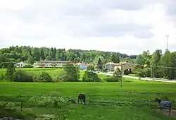 A far shot of the area. Very green field with a town in the distance. Many trees further than that.
