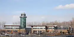 Across a parking lot is a two-story building with a circular tower that is offset from the center of the building.